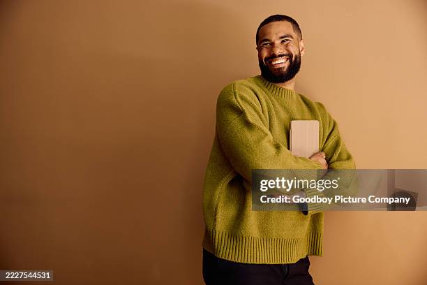 cheerful young business man holding a digital tablet while standing against a plain brown wall in a minimalist office - smart casual stock pictures, royalty-free photos & images