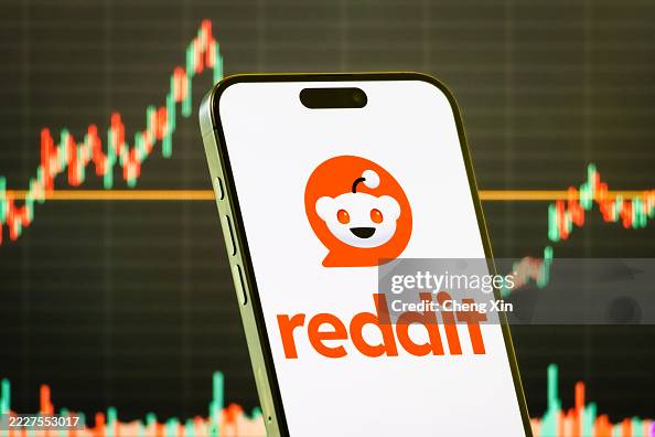 Reddit Inc. logo displayed on smartphone screen with stock market chart in background Reddit Inc. logo displayed on smartphone screen with stock market chart in background