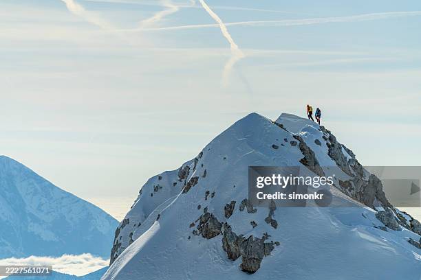 adventurous mountaineers standing on snow-covered mountain summit under clear sky - mountain ridge stock pictures, royalty-free photos & images