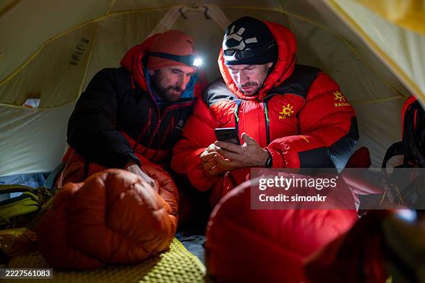 experienced mountaineers using smartphone inside a cozy alpine tent at high altitude - base camp stock pictures, royalty-free photos & images