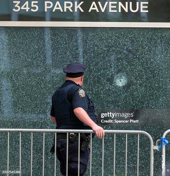New York Police Department officer stands in front of a bullet-shattered window at 345 Park Avenue building on Park Avenue after a gunman killed four...