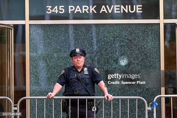 New York Police Department officer stands in front of a bullet-shattered window at 345 Park Avenue building on Park Avenue after a gunman killed four...