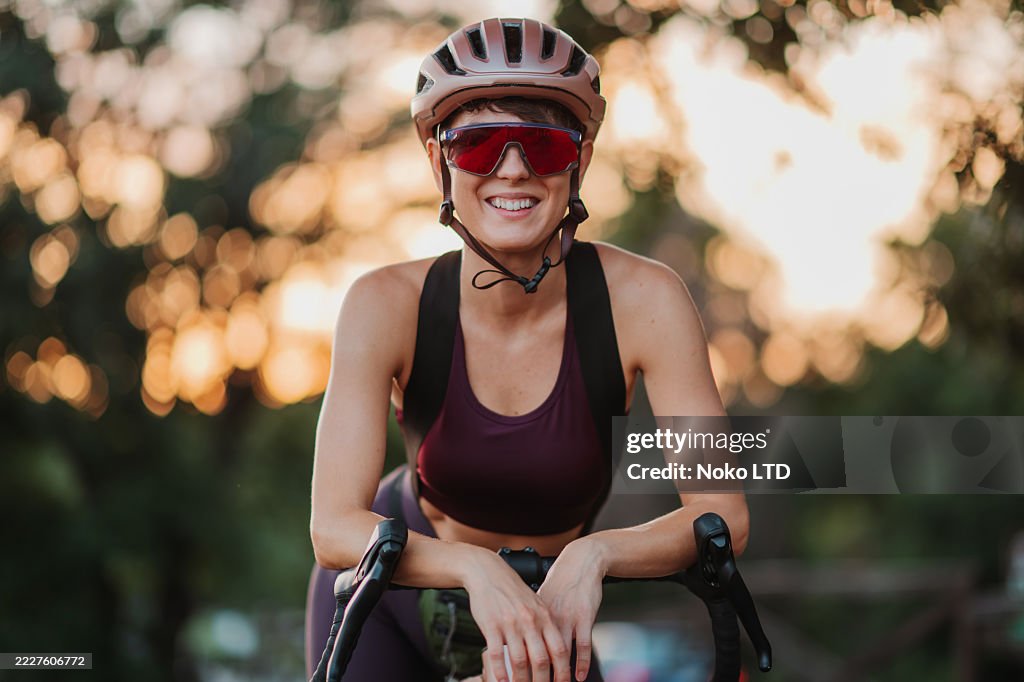 Young female cyclist smiling at camera during sunset