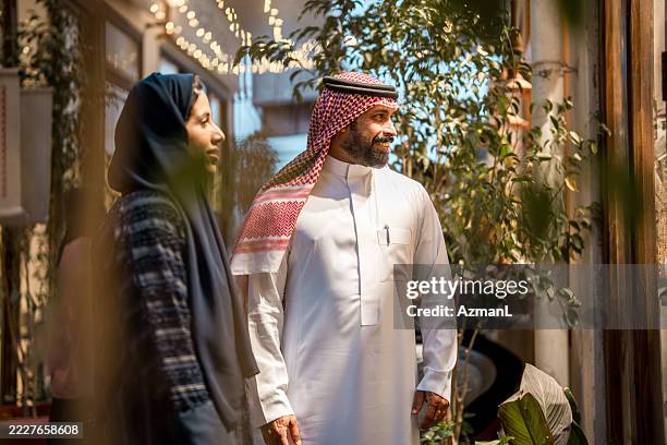 couple du moyen-orient en robe traditionnelle marchant dans un jardin intérieur ensoleillé - culture saoudienne photos et images de collection