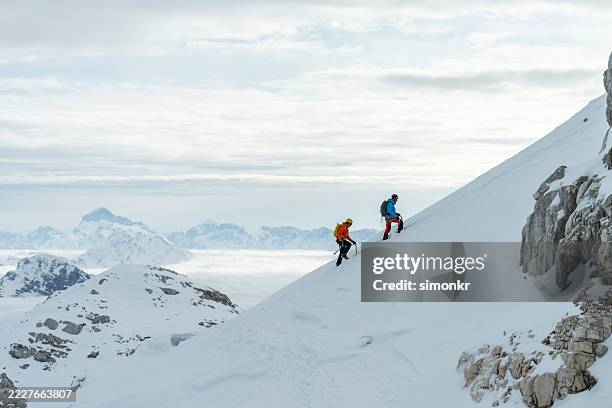 two mountaineers ascending steep snow slope during winter alpine expedition - adventure stock pictures, royalty-free photos & images