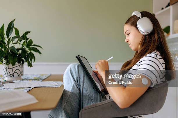 teenage girl doing homework with diabetic sensor on her arm - type 1 diabetes stock pictures, royalty-free photos & images