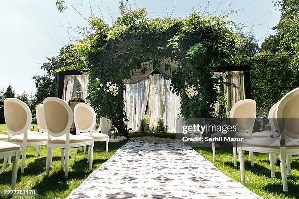 elegant outdoor wedding setup featuring a floral arch and white chairs in a lush garden during the daytime. - wedding planning foto e immagini stock