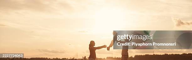 asian family enjoying outdoor time at sunset. father playing lifts child in the air while mother reaches out, creating a heartwarming moment of love, care, and togetherness in golden light. - life insurance stock pictures, royalty-free photos & images