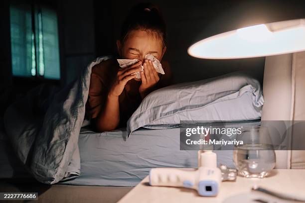 a girl with a cold or flu is lying in bed. there are many medications in the foreground. - cold virus stock pictures, royalty-free photos & images
