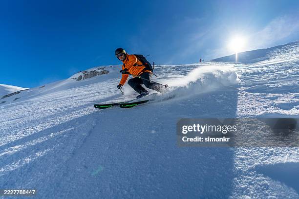 male ski mountaineer descending snowy mountain under bright blue sky - professional skier stock pictures, royalty-free photos & images