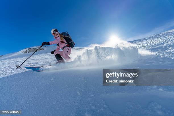 female ski tourer descending snowy mountain in bright sunlight - professional skier stock pictures, royalty-free photos & images