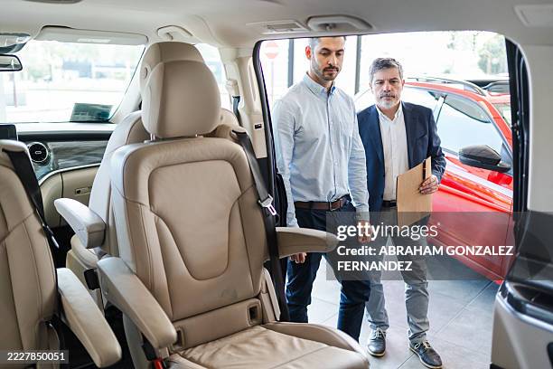 salesperson demonstrating the interior features of a minivan to a potential buyer in a bustling car dealership showroom - used car selling stock pictures, royalty-free photos & images