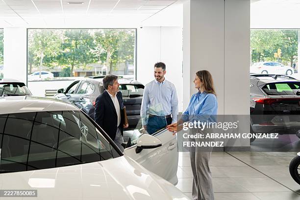 saleswoman showing new car features to a couple in a dealership, discussing financing options and purchase agreements - electric car display stock pictures, royalty-free photos & images