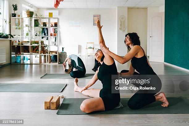 yoga teacher helping student performing stretching exercise in studio - mat stock pictures, royalty-free photos & images