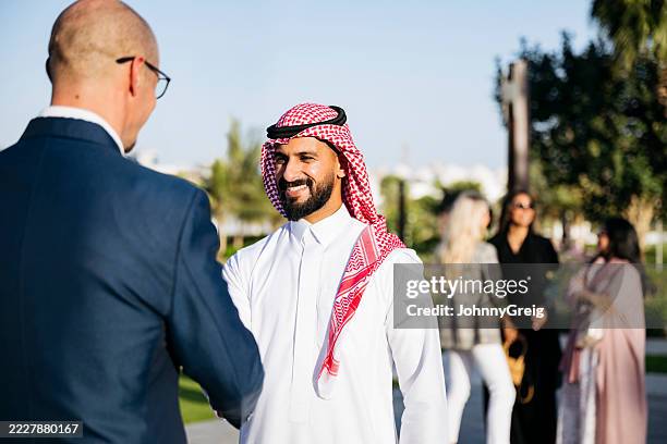 cheerful middle eastern businessman smiling and shaking hands with caucasian partner - saudi people stock pictures, royalty-free photos & images
