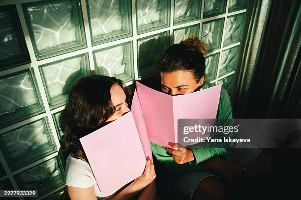 two friends enjoying a vibrant moment with menus in cozy cafe lighting - cotilleo fotografías e imágenes de stock