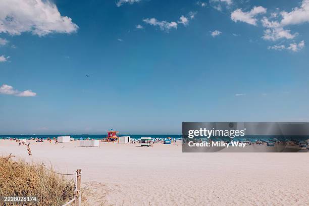 miami sandy beach with people, sun umbrellas, and a lifeguard tower. clear blue sky. - miami beach stock pictures, royalty-free photos & images