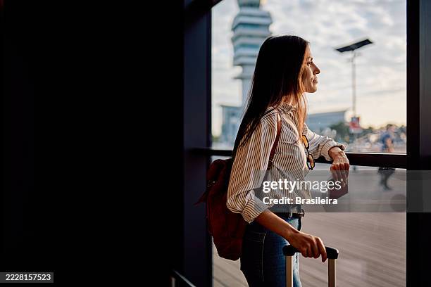 young woman waiting at the airport contemplating the view - airport window stock pictures, royalty-free photos & images