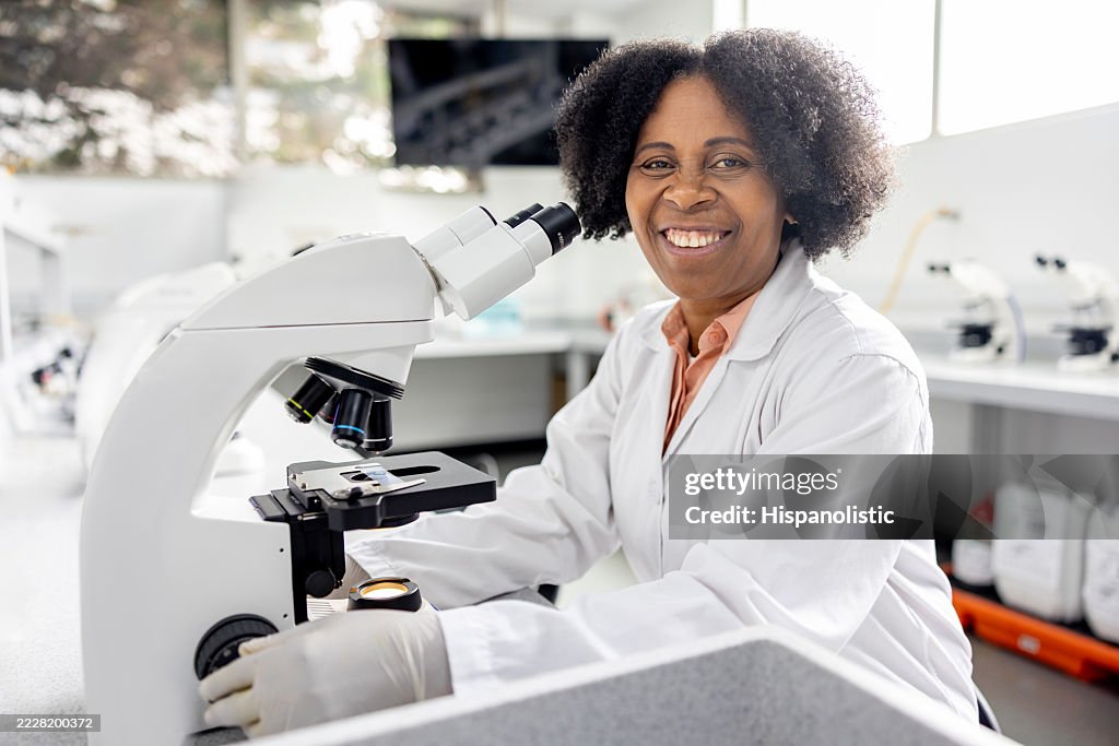 Glücklicher Wissenschaftler, der im Labor lächelt, während er ein Mikroskop benutzt