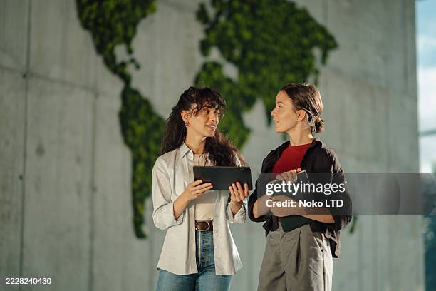 two young businesswomen discussing a project using digital tablet and notebook - sustainable business stock pictures, royalty-free photos & images