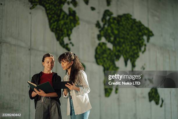 two young women discussing global issues near moss world map - global village stock pictures, royalty-free photos & images