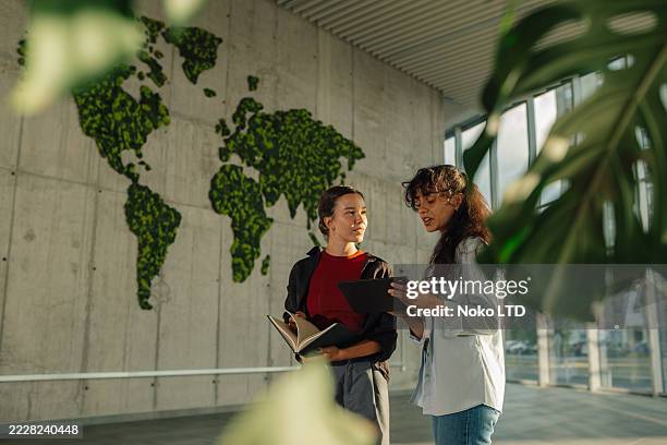 dos jóvenes empresarias discutiendo junto a un mapamundi verde hecho de musgo - ecosistema fotografías e imágenes de stock