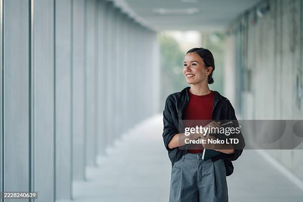 smiling young woman walking through office hallway holding notebook - anticipation stock pictures, royalty-free photos & images