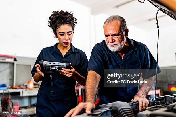mechaniker sprechen und untersuchen das auto in der autowerkstatt - stereotypische geschlechtsrolle stock-fotos und bilder