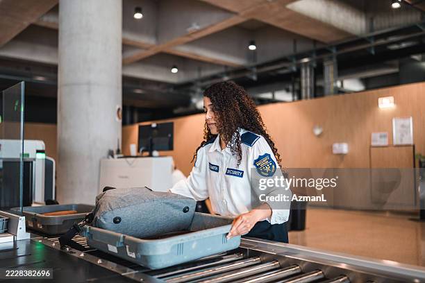 joven oficial de seguridad aeroportuaria hispana inspeccionando equipaje en uniforme - agencia nacional de transporte fotografías e imágenes de stock