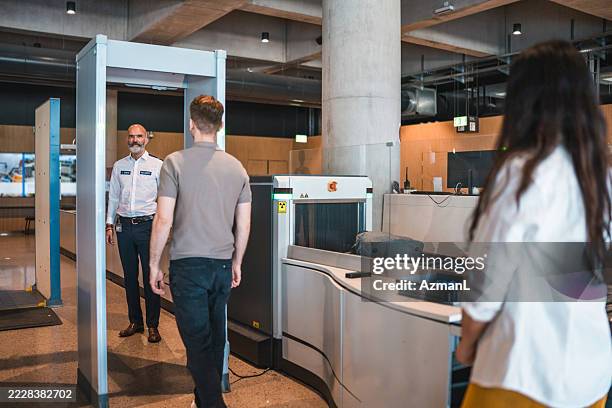 male passenger walking through airport security checkpoint with smiling security officer - airport border control stock pictures, royalty-free photos & images