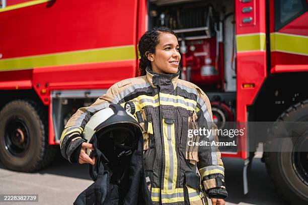junge hispanische feuerwehrfrau in voller montur steht selbstbewusst in der nähe eines flughafen-feuerwehrautos - feuerwehrmann stock-fotos und bilder