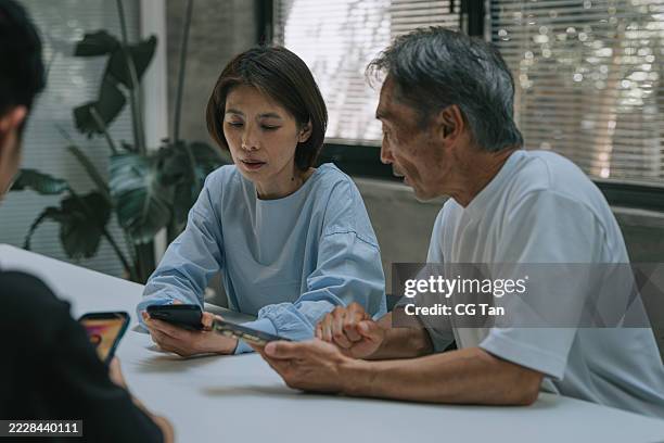 mulher japonesa de meia-idade e homem mais velho discutindo conteúdo digital em smartphones no escritório moderno - diferença entre gerações - fotografias e filmes do acervo