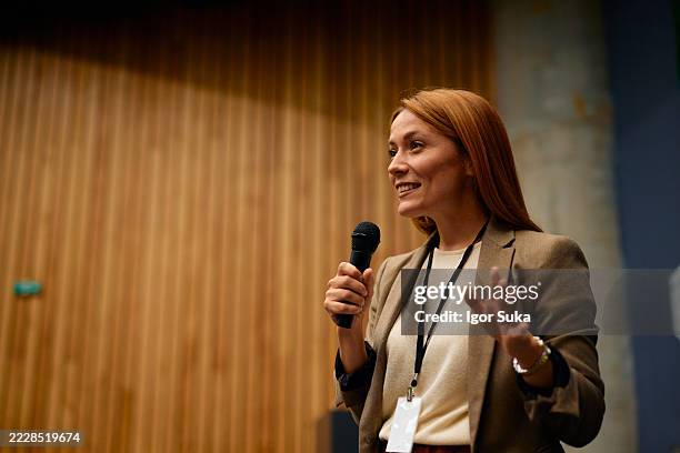 confident businesswoman speaking at a conference, holding a microphone - luidspreker stockfoto's en -beelden