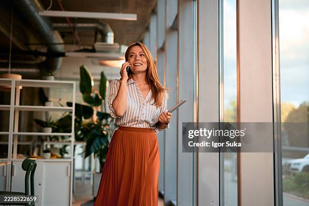 businesswoman walking and talking on the phone in a modern office - skirt stock pictures, royalty-free photos & images