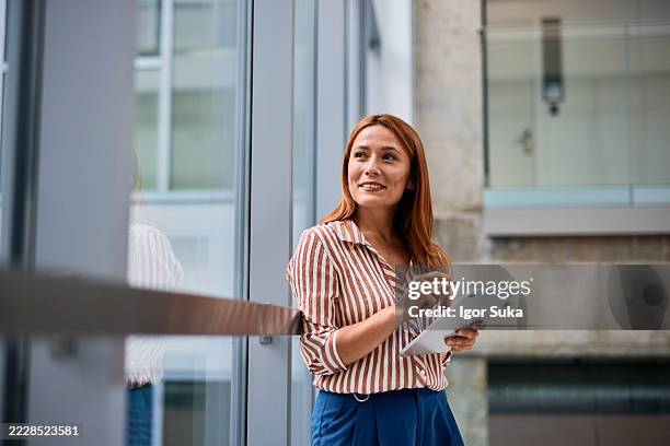 businesswoman using digital tablet and looking away in modern office building - leaning stock pictures, royalty-free photos & images
