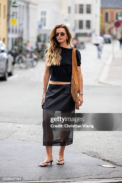 Guest wears black transparent skirt, brown suede bag with fringes, black shirt outside Freya Dalsjø during Copenhagen Fashion Week day one on August...