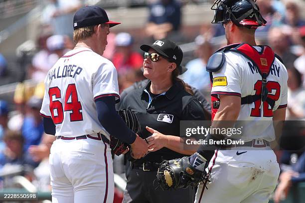 Umpire Jen Pawol inspects the glove of Hurston Waldrep of the Atlanta Braves as Sean Murphy looks on in the first inning of a game against the Miami...