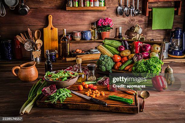 making a vegan salad in rustic kitchen with assorted organic vegetables. natural window lighting - red bell pepper stock pictures, royalty-free photos & images