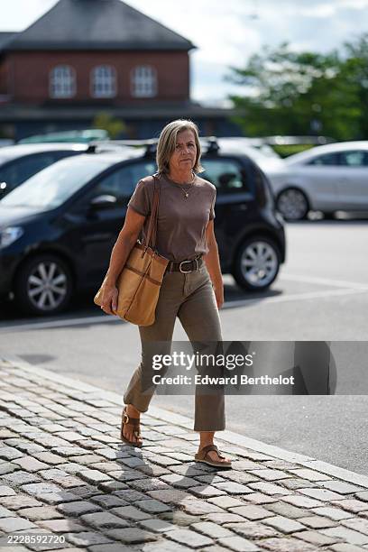 Guest wears a brown short-sleeve t-shirt paired with taupe cropped pants. A brown leather belt is visible at the waist. The outfit is accessorized...