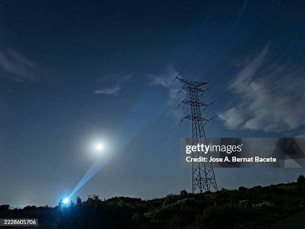 a high-voltage tower on a mountain with an electrician carrying flashlights repairing a fault at night. - apagão imagens e fotografias de stock