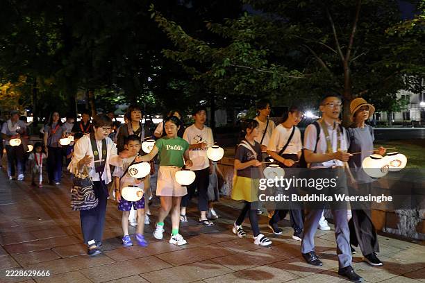 People carry lanterns and walk commemorating the atomic bombing of Hiroshima ahead of the 80th anniversary at the Hiroshima Peace Memorial Park on...