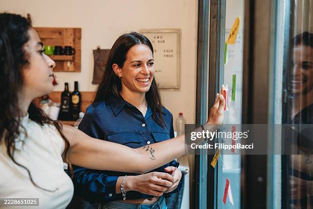 due giovani imprenditrici che usano post-it durante una sessione di brainstorming - direttrice foto e immagini stock