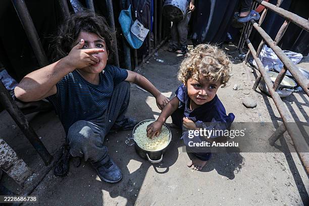 Palestinians wait with pots in their hands as a charitable organization distributes food to Palestinians suffering food crisis under Israeli blockade...