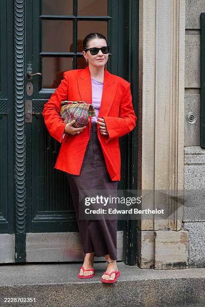 Guest wears a bright red blazer with structured shoulders and a relaxed fit over a light purple top. Sunglasses with dark lenses and a black frame...
