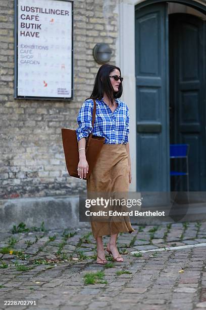 Guest wears a blue and white plaid button-up shirt with rolled-up sleeves. The shirt is tucked into a high-waisted, camel-colored suede skirt that...