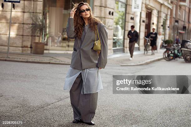 Guest wears grey suit made of pants and oversized blazer, sheer skirt and green bag outside Tekla breakfast during Copenhagen Fashion Week day two on...
