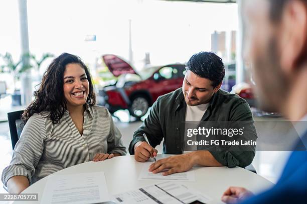 couple signing documents at car dealership - autokredit stock-fotos und bilder