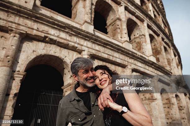senior tourists smiling in front of the colosseum - coliseum rome stock pictures, royalty-free photos & images