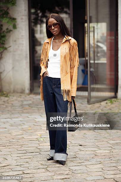 Guest wears navy blue jeans, white Loewe top, brown suede jacket with tassels and black Celine bag outside the Skall Studio show during Copenhagen...