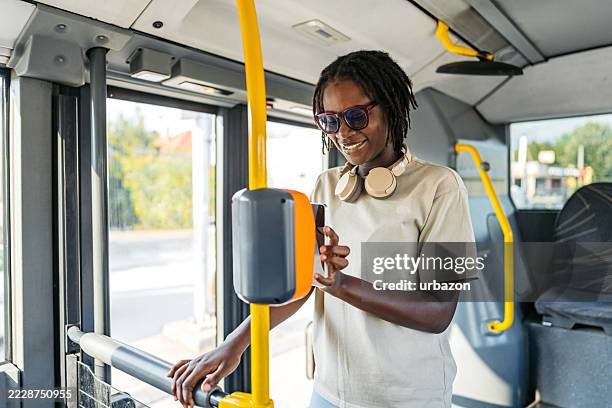 young black woman checking her e-ticket with a phone in a public bus - contactless payment bus stock pictures, royalty-free photos & images